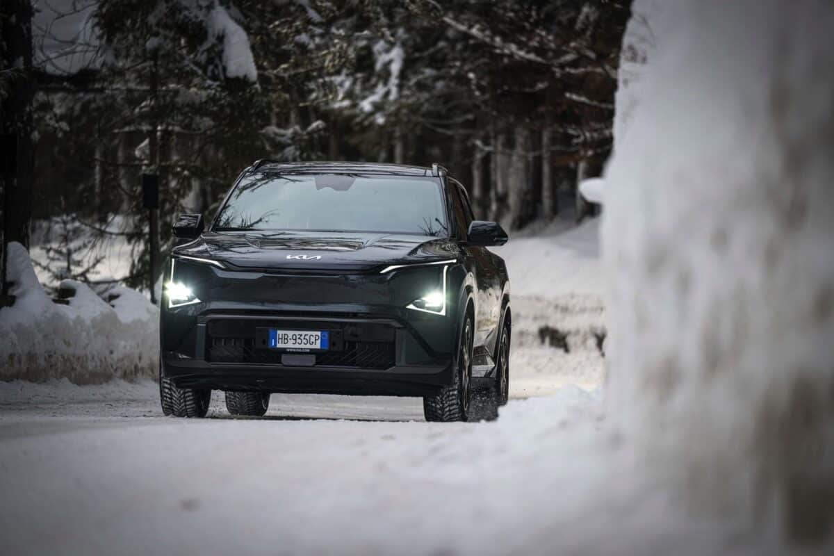 Auto nera Kia EV5 su strada innevata, ambiente boschivo, vista frontale di giorno.