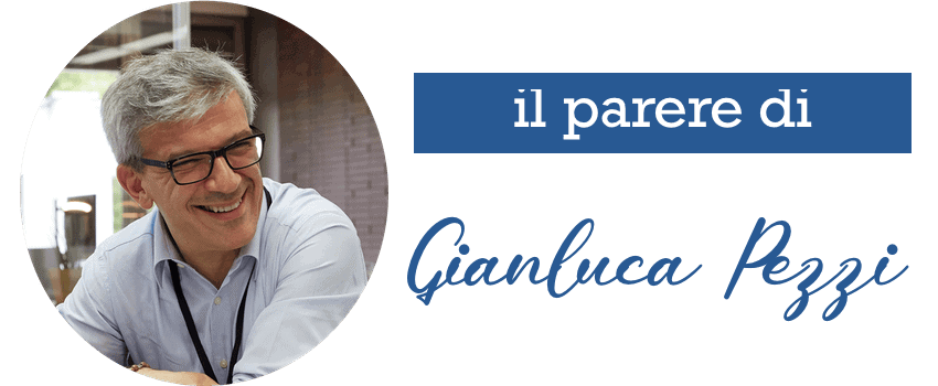 Gianluca Pezzi sorride, indossando una camicia chiara e occhiali, in un ambiente interno illuminato.